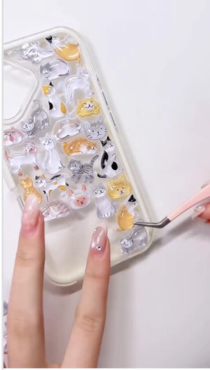 Handcrafted clear phone case with a white border, densely decorated with a 3D collage of glossy, transparent cartoon cat charms including calico, orange tabby, and grey stripes.