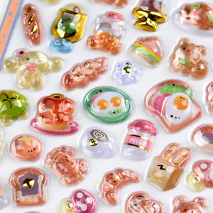 Close-up of 3D crystal clear stickers with adorable bakery and dessert designs (bread, croissant, egg toast), featuring gold foil and iridescent effects