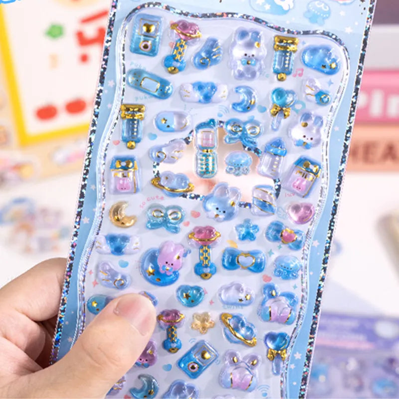 Handheld display of 3D crystal puffy sticker sheets with cute blue pet and gadget designs, featuring gold foil and iridescent effects