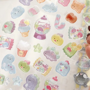 Close-up shot of 3D puffy stickers with dinosaur, gumball machine, and candy packaging designs, highlighting the transparent iridescent texture and cute details