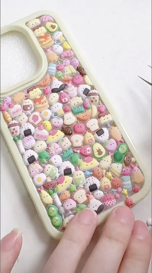 Finished DIY iPhone case with cream frame, decorated with dense mini dessert, snack, and cute character stickers in pastel colors, creating a cozy sweet aesthetic.