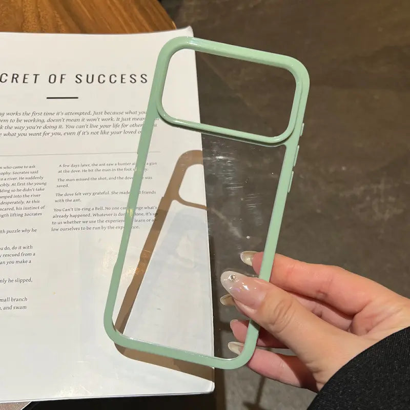 Minimalist pastel green contrast bumper phone case with a clear transparent back, held over a book background.