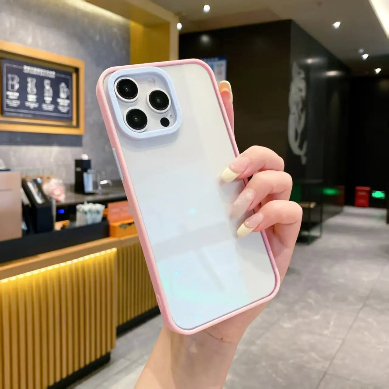 A minimalist pastel pink hybrid phone case featuring a baby blue contrast camera lens protective ring and a crystal clear transparent back, held in hand.