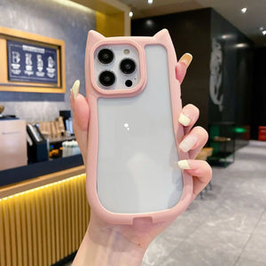 A unique hybrid protective phone case in pastel pink featuring a custom cat-ear shape top border and a crystal clear transparent back panel, shown held in hand.