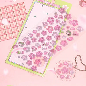 Decorative display of 3D sakura crystal stickers used for journal and keychain DIY, featuring cherry blossom and fruit designs, perfect for spring-themed crafts