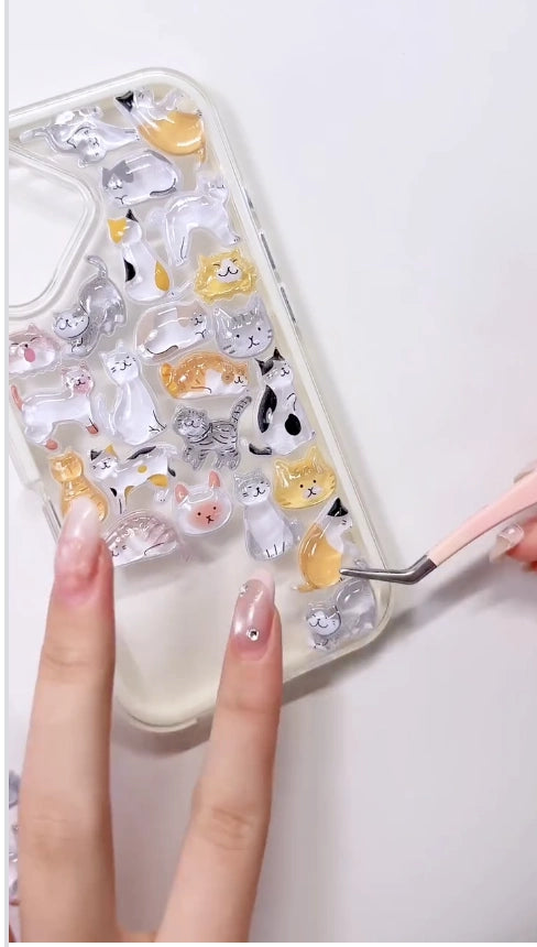 Handcrafted clear phone case with a white border, densely decorated with a 3D collage of glossy, transparent cartoon cat charms including calico, orange tabby, and grey stripes.