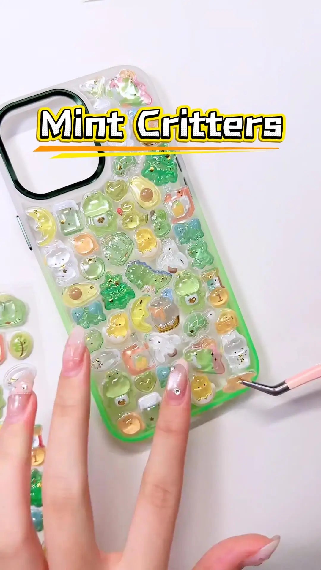 Handcrafted phone case with a mint green frame, densely filled with a 3D collage of glossy, transparent green frog charms, cartoon dinosaurs, split avocados, and golden crescent moons.