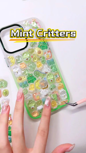 Handcrafted phone case with a mint green frame, densely filled with a 3D collage of glossy, transparent green frog charms, cartoon dinosaurs, split avocados, and golden crescent moons.