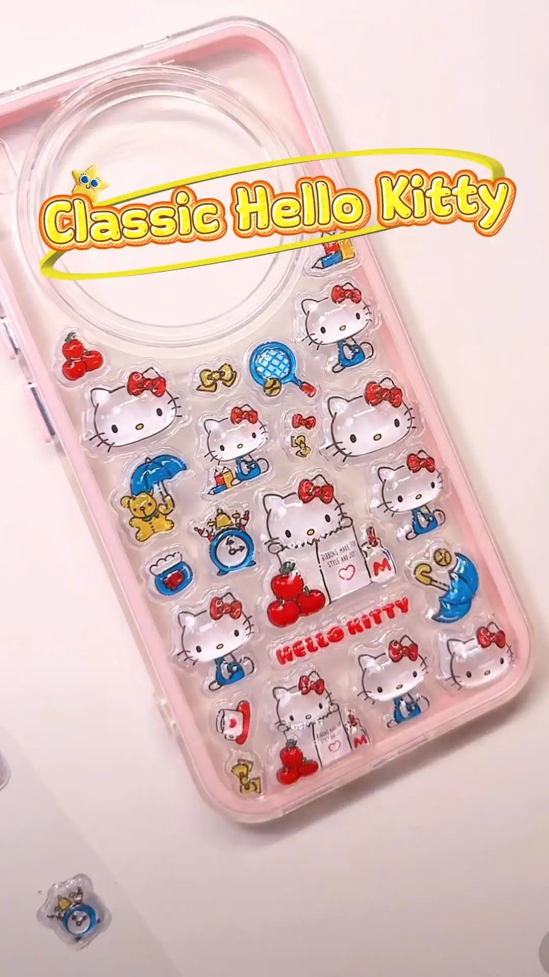 Handcrafted clear pastel pink phone case featuring a dense 3D collage of classic Hello Kitty cartoon charms, red apples, and blue umbrellas.