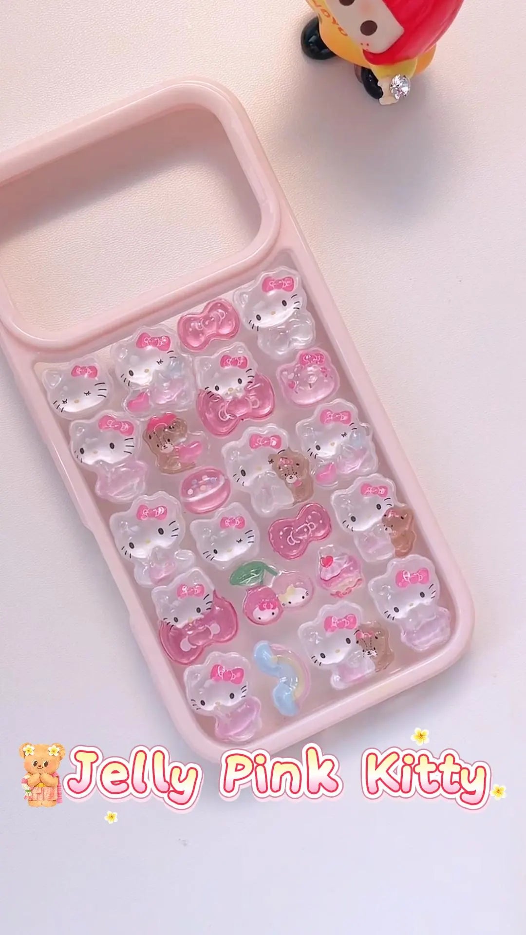 Handcrafted phone case with a pastel pink frame filled with a dense 3D collage of glossy, semi-transparent Hello Kitty charms, pink bows, and cherries.
