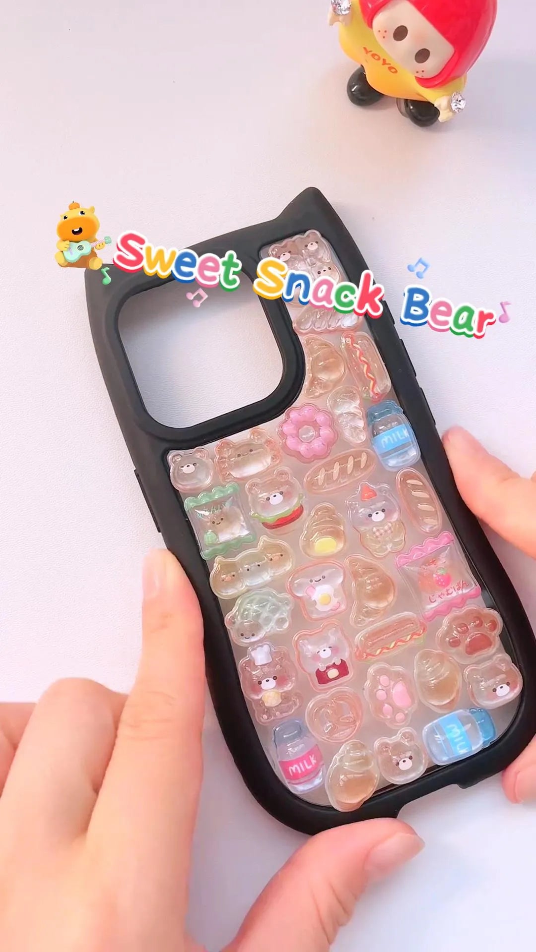 Handcrafted phone case with a matte black cat-ear shaped border, densely filled with a 3D collage of glossy, amber caramel cartoon chef bear charms, miniature croissants, and donuts.
