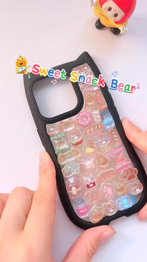 Handcrafted phone case with a matte black cat-ear shaped border, densely filled with a 3D collage of glossy, amber caramel cartoon chef bear charms, miniature croissants, and donuts.