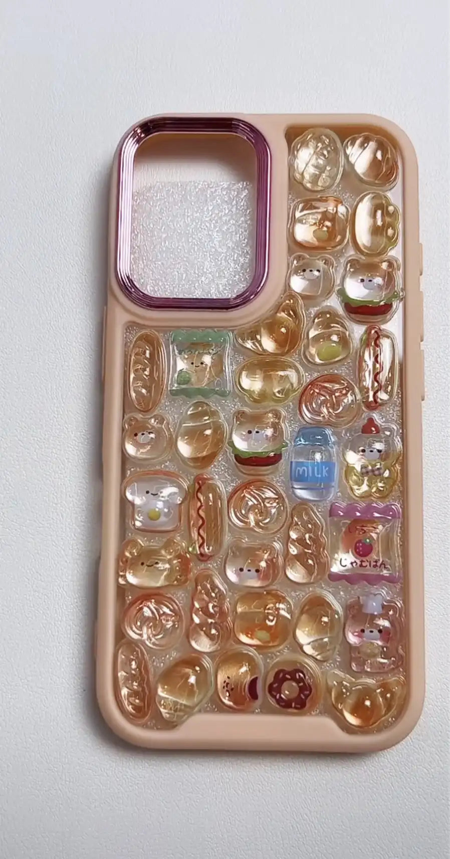 Finished DIY iPhone case with pink frame, decorated with glossy Bonbon Drop bread, dessert, and bear stickers, featuring warm amber jelly-style designs.