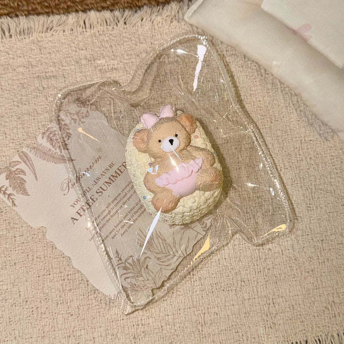 Toast-shaped squishy with a knit-like texture, bear figure and pink bow in clear packaging.