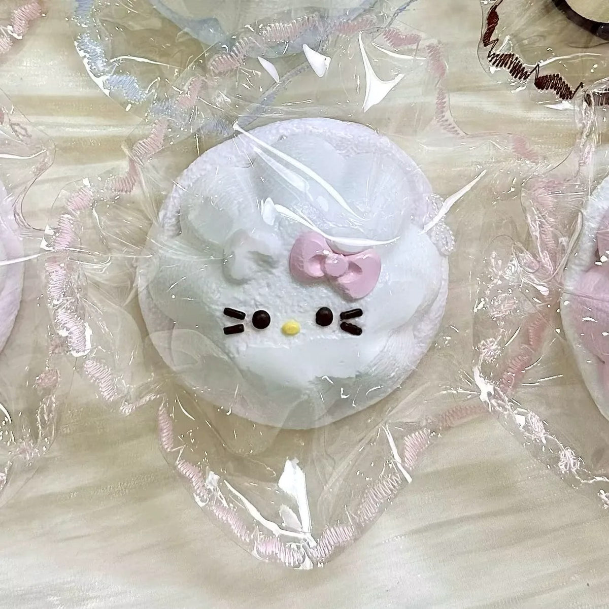 White cat-face pudding squishy with a pink bow in clear packaging.