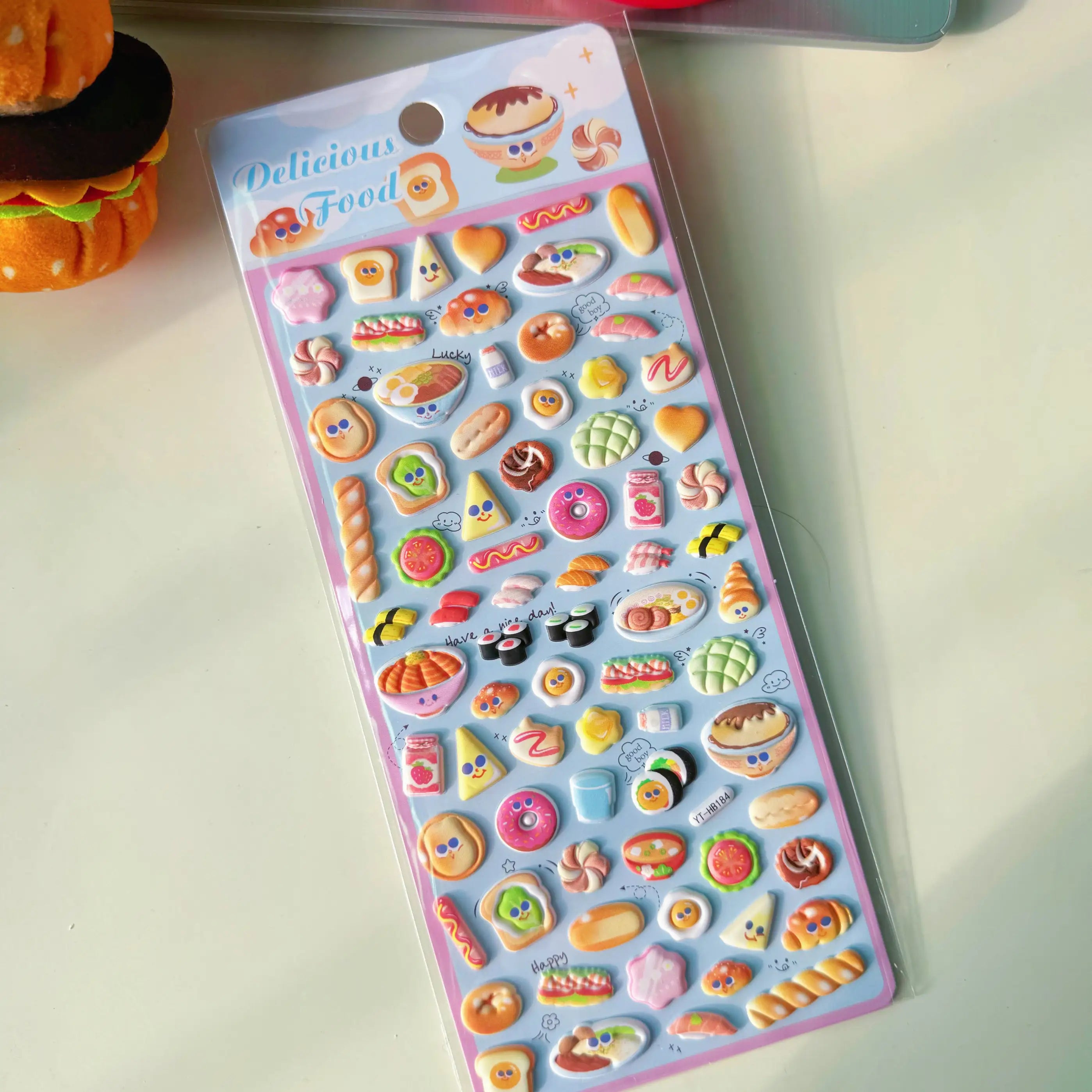 Delicious Food" cute kawaii sticker sheet in light blue tone, with glossy cartoon food designs (sushi, bread, donuts, etc.), ideal for craft decoration.