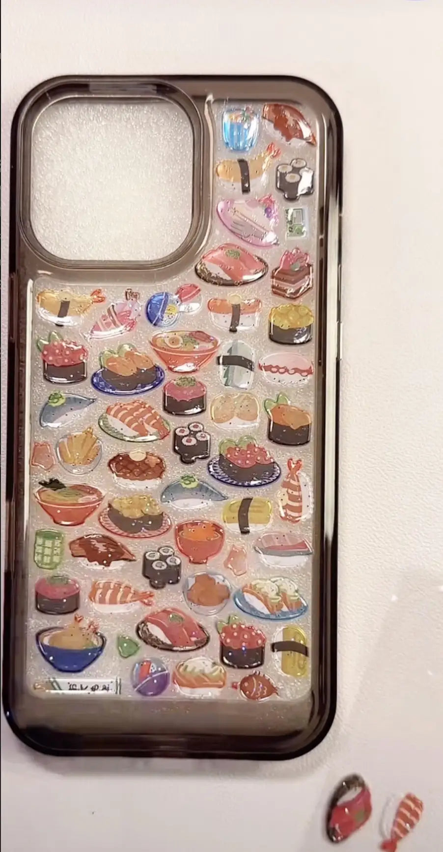 Finished DIY iPhone case with smoky black frame, decorated with glossy Bonbon Drop sushi and Japanese food stickers, creating a vibrant Japanese cuisine aesthetic.