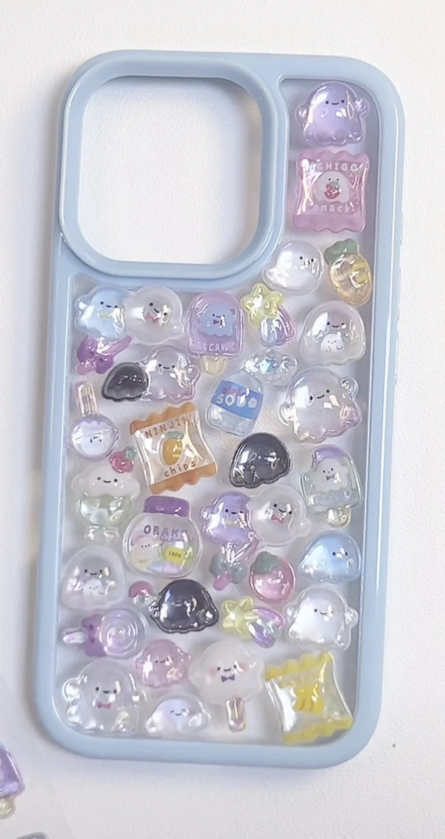 Finished DIY iPhone case with light blue frame, decorated with glossy pastel ghost and snack jelly stickers, creating a dreamy whimsical aesthetic.