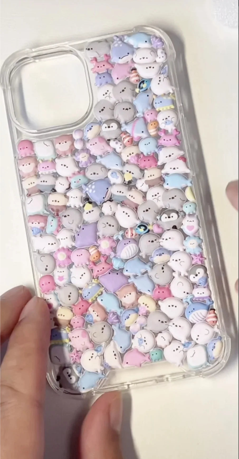 Finished DIY clear iPhone case decorated with a dense array of cute pastel sea creature stickers, including seals, penguins, and other kawaii marine animals.