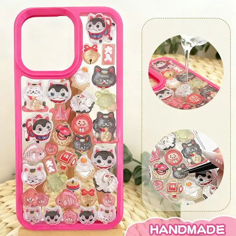Finished DIY iPhone case with hot pink frame, decorated with dense glossy lucky cat and daruma stickers, creating a festive and lucky aesthetic.