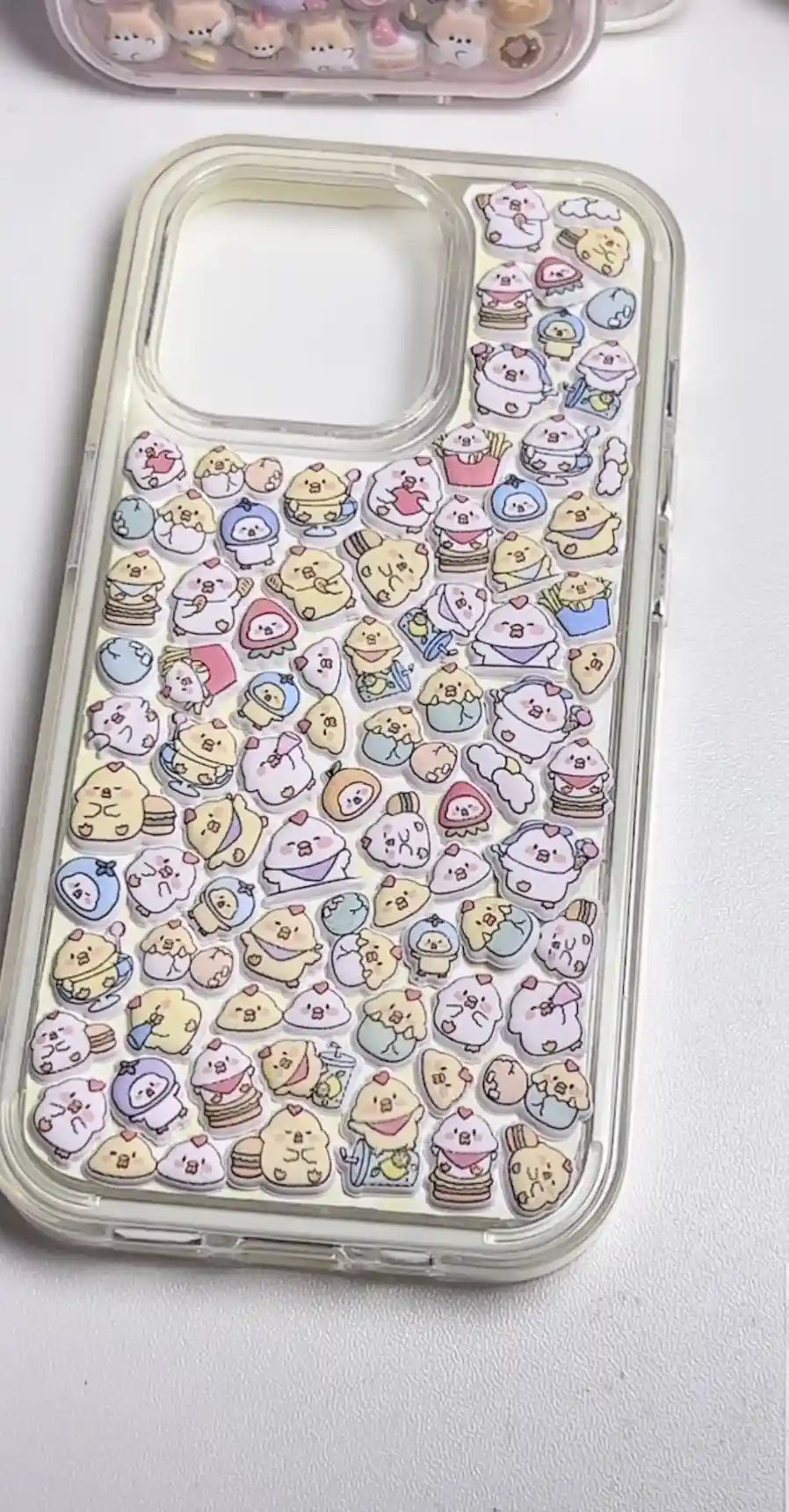 Finished DIY clear iPhone case decorated with dense mini chick and cute animal stickers, featuring a pastel colorful kawaii aesthetic.
