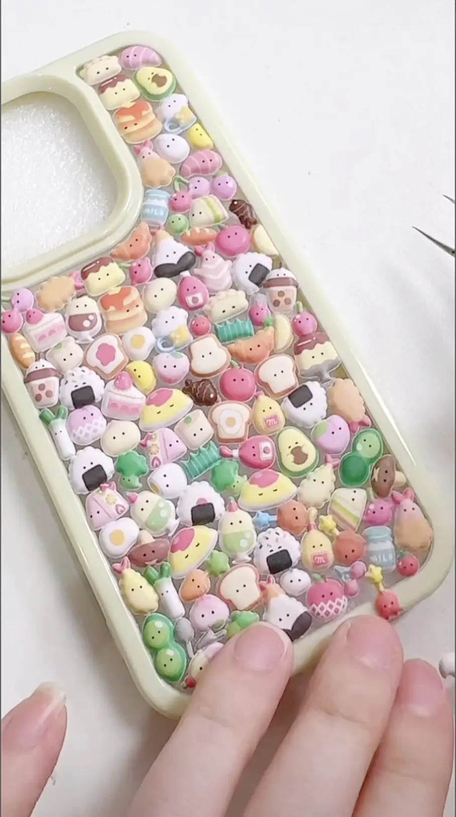 Finished DIY iPhone case with cream frame, decorated with dense mini dessert, snack, and cute character stickers in pastel colors, creating a cozy sweet aesthetic.

