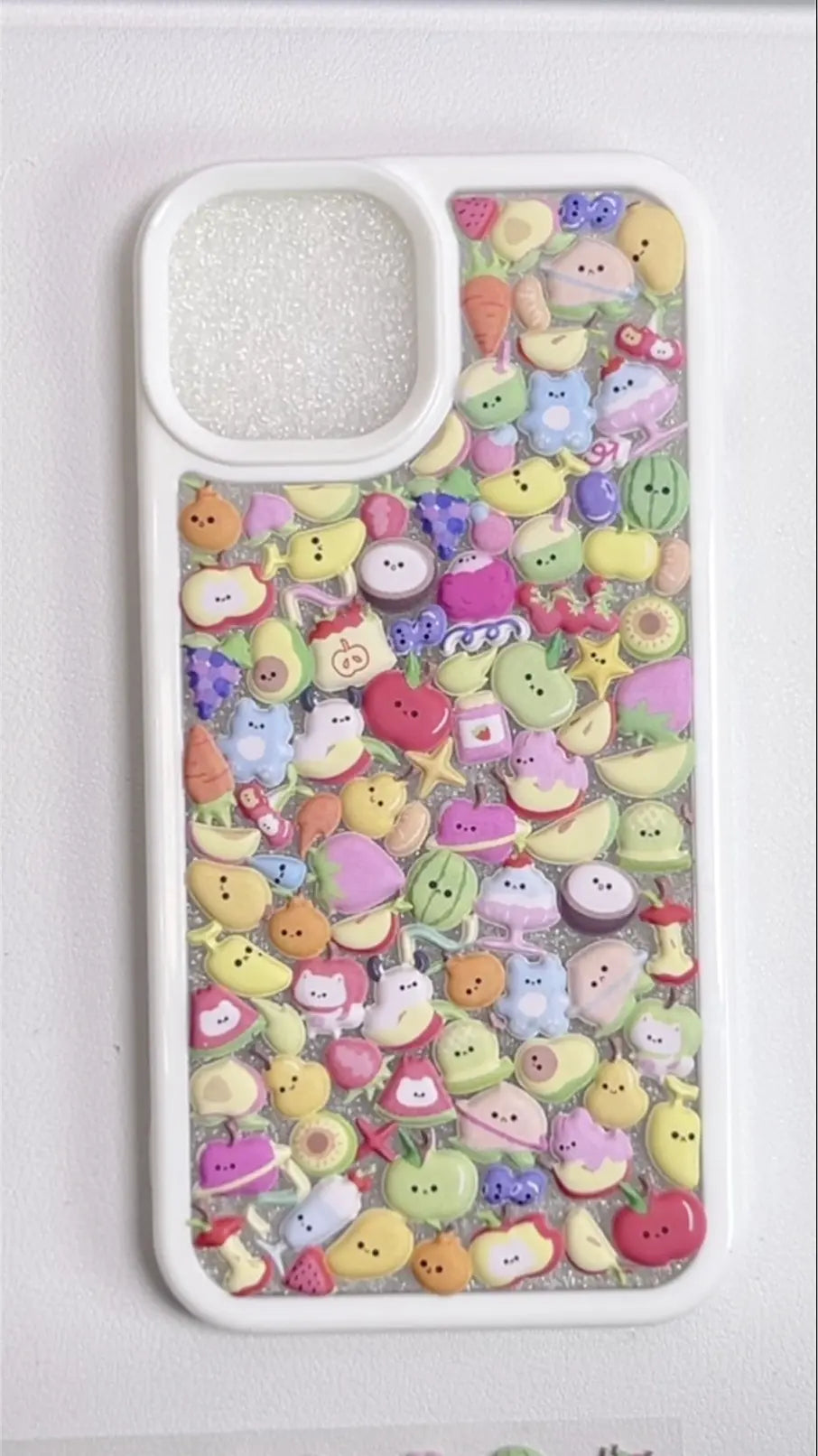 Finished DIY iPhone case with white frame, decorated with dense mini fruit and cute character stickers in pastel colors, creating a fresh fruity aesthetic.
