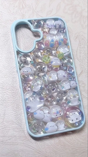 Finished DIY iPhone case with light blue frame, decorated with dense glittery POP SEAL Shimaenaga bird stickers, featuring a dreamy iridescent jelly aesthetic.