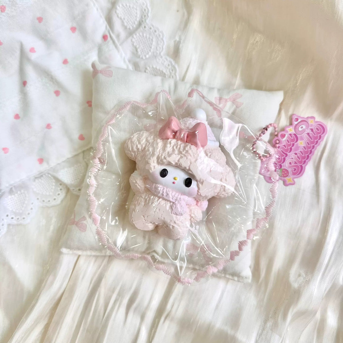 White lamb-shaped squishy with a textured surface and pink bows in clear packaging.