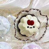 Cream-colored pudding squishy with a red detail and dark base in clear packaging.