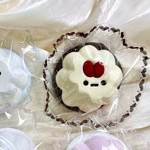 Cream-colored pudding squishy with a red detail and dark base in clear packaging.