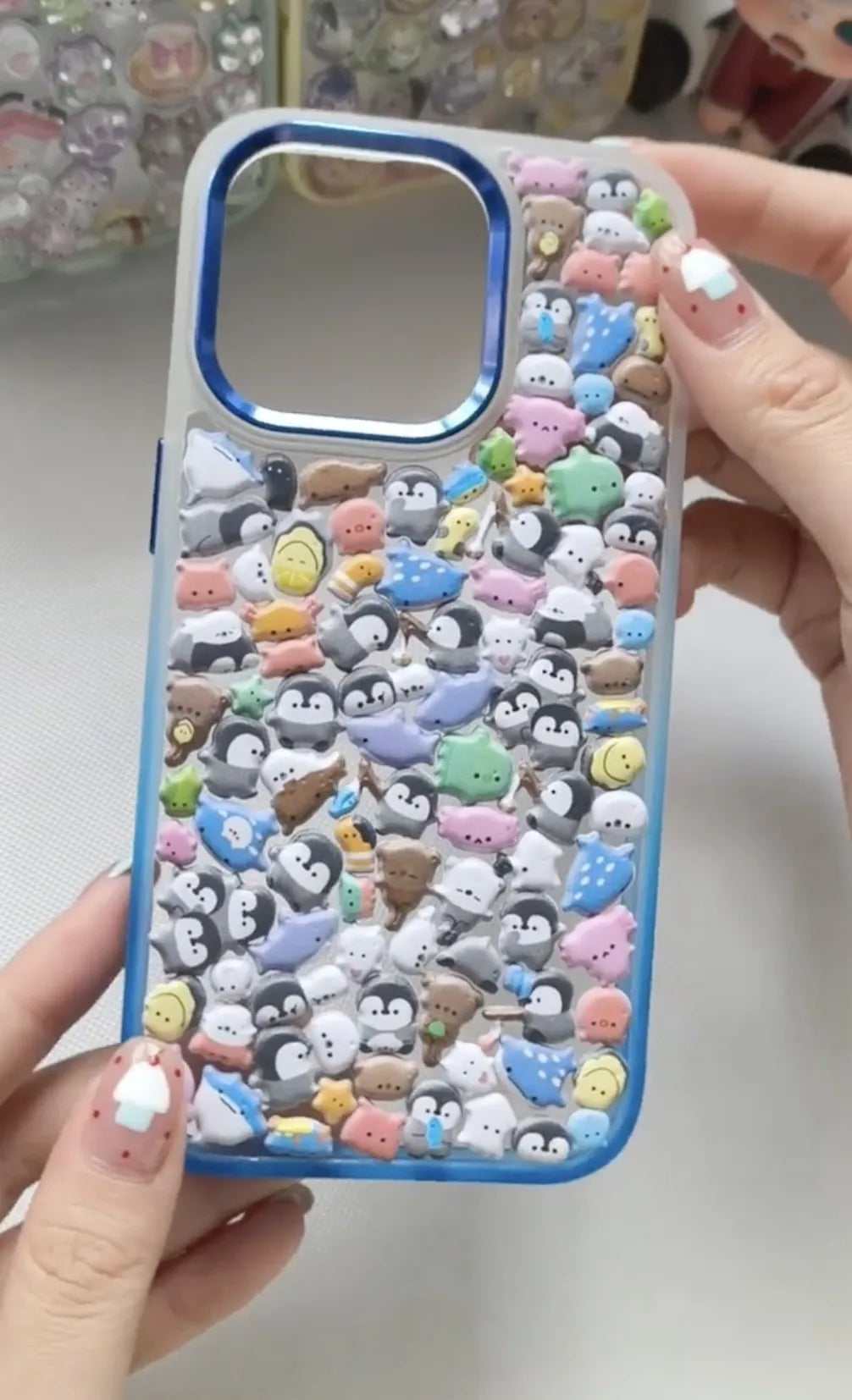 Final product of a handmade DIY phone case featuring 3D resin penguins and summer dessert charms on a white wave-edge frame.