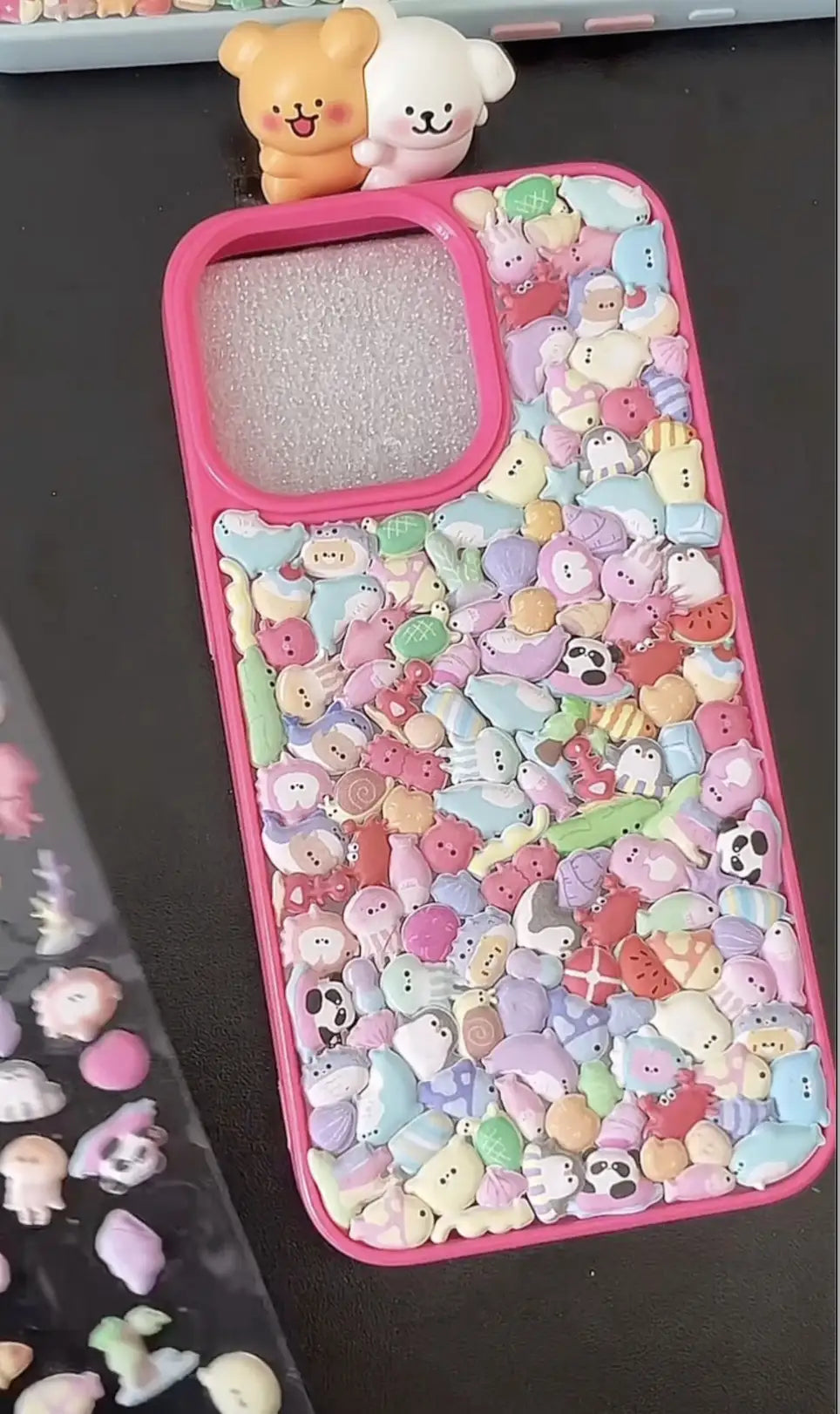 Final look of a handmade DIY phone case covered in 3D transparent pink hearts and black punk charms, cyber kawaii aesthetic.