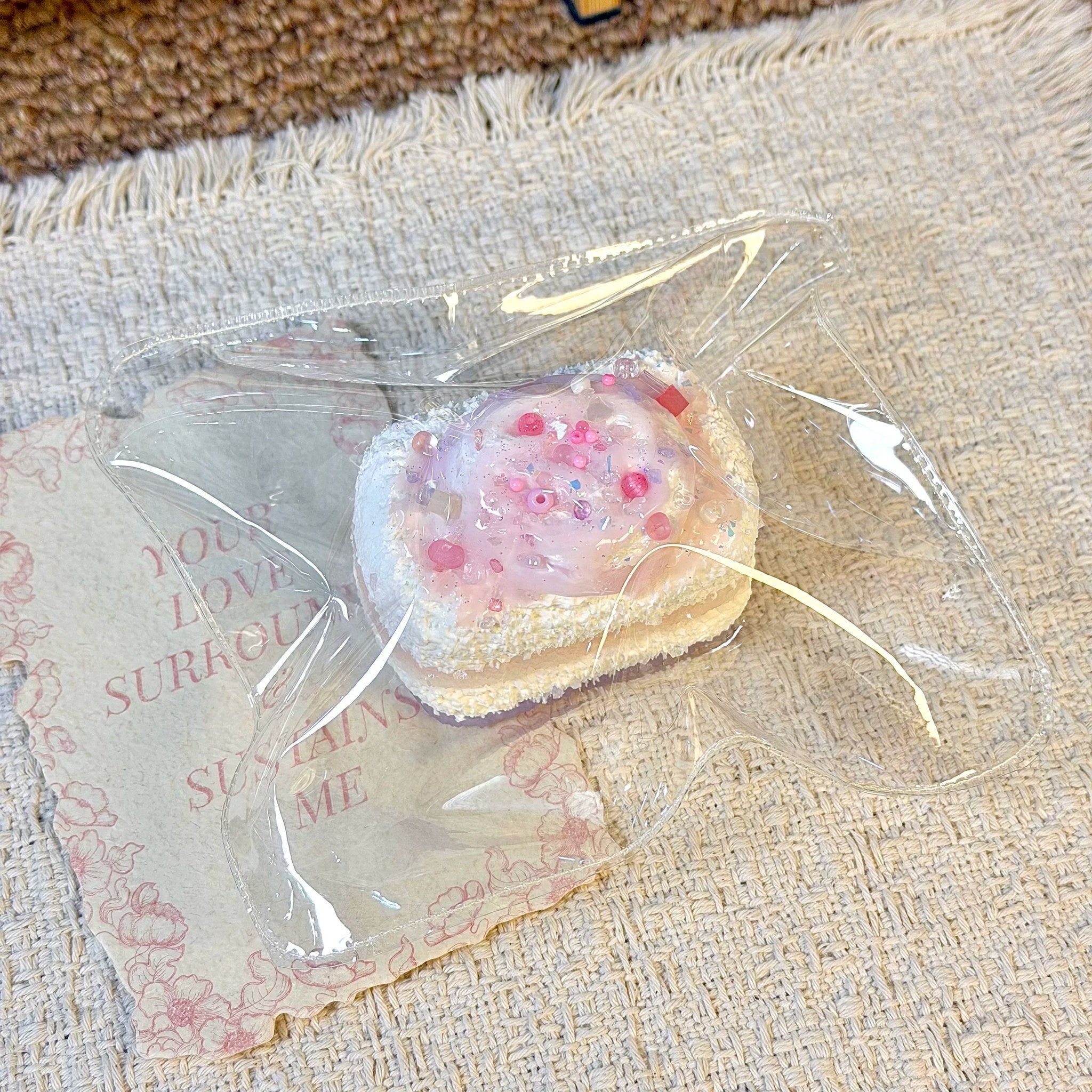 Bread-shaped squishy with white topping and pink details in clear packaging.