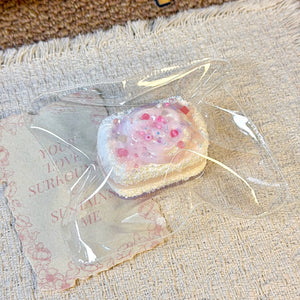 Bread-shaped squishy with white topping and pink details in clear packaging.