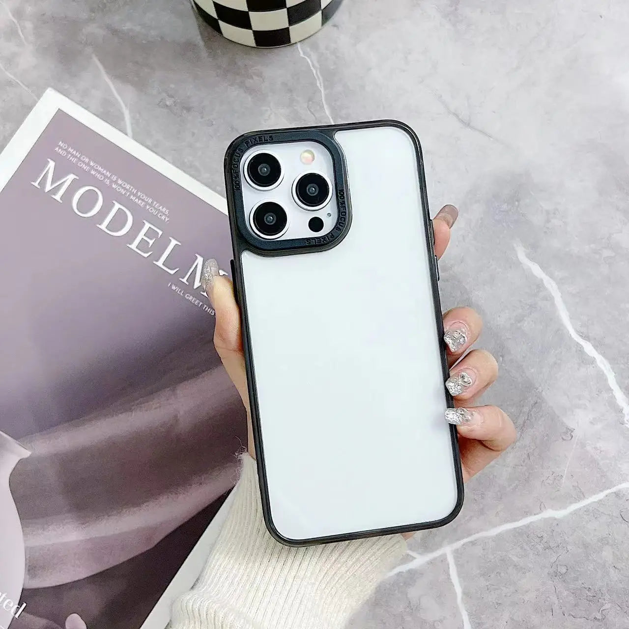 A minimalist hybrid protective phone case in sleek black featuring a raised camera bezel and a crystal clear transparent back panel, shown held in hand.