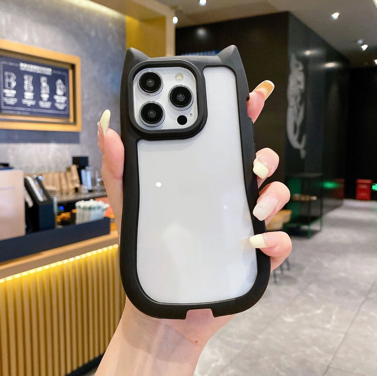 A unique hybrid protective phone case in matte black featuring a custom cat-ear shape top border and a crystal clear transparent back panel, shown held in hand.