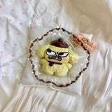 Yellow textured dog-shaped squishy with a brown hat and mischievous face in clear packaging.