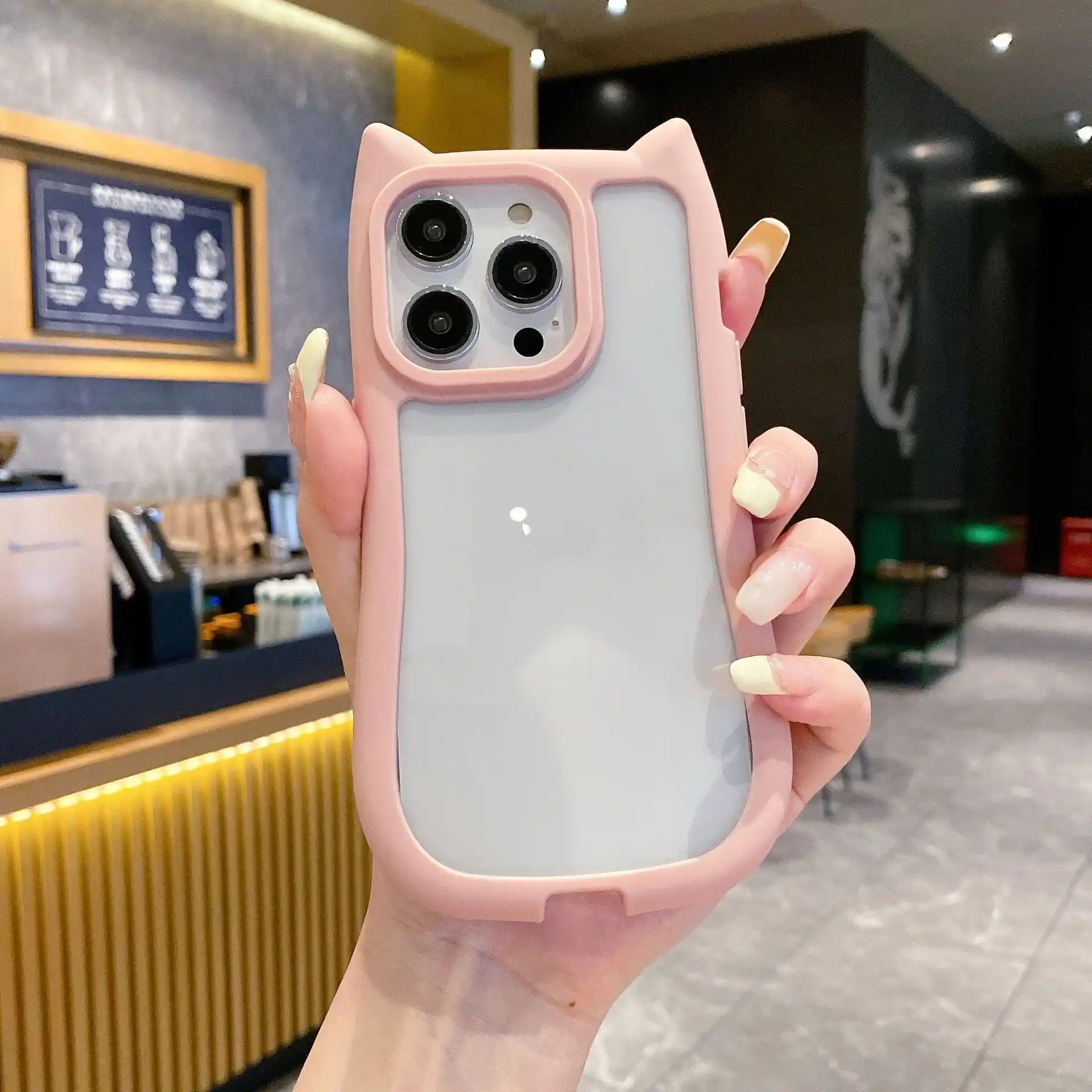 A unique hybrid protective phone case in pastel pink featuring a custom cat-ear shape top border and a crystal clear transparent back panel, shown held in hand.