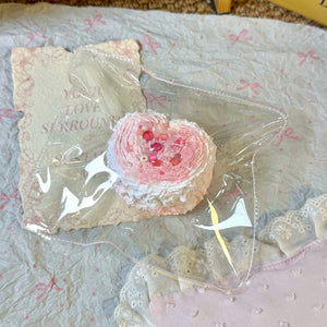 Pink heart-shaped pastry squishy with a textured surface in clear packaging.