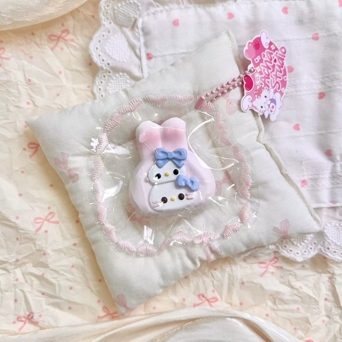White cat-shaped squishy wearing a pink long-eared hood in clear packaging.