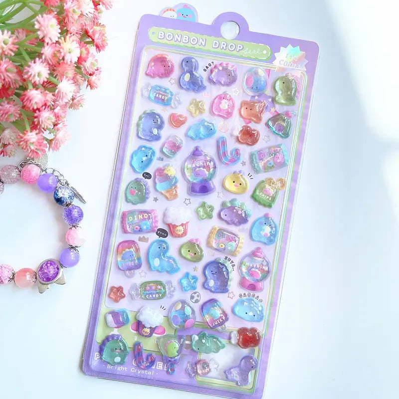 Scene display of purple dinosaur themed "BONBON DROP" 3D crystal puffy sticker sheet, featuring cute dinosaur, candy, and gumball machine designs with iridescent effects