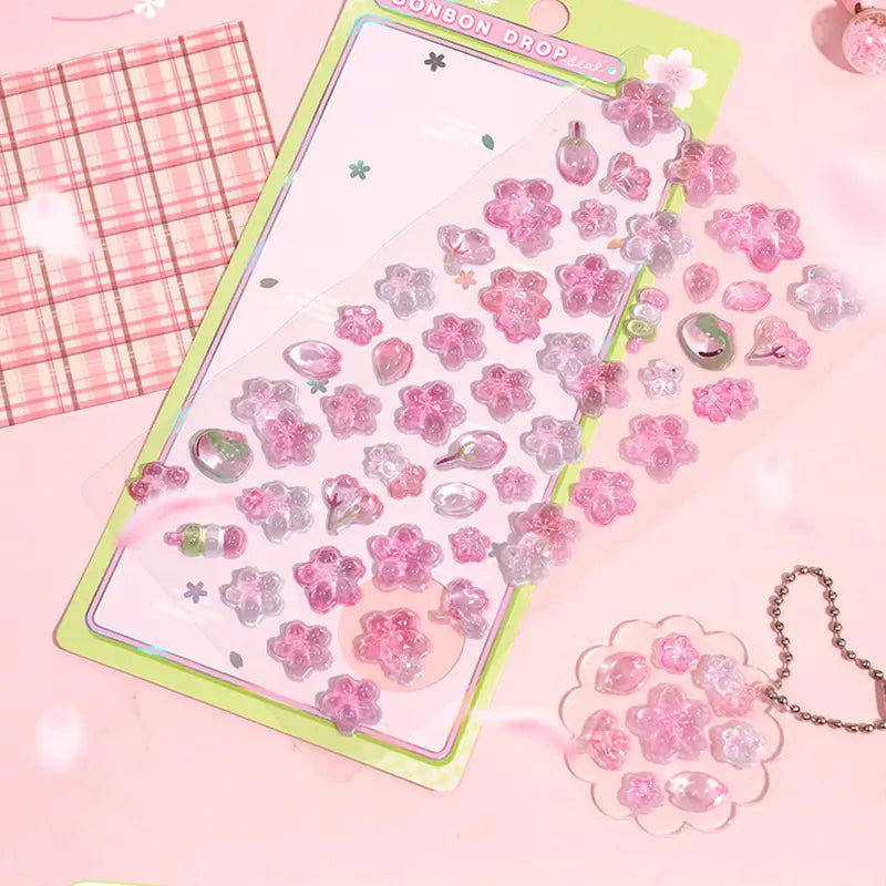 Decorative display of 3D sakura crystal stickers used for journal and keychain DIY, featuring cherry blossom and fruit designs, perfect for spring-themed crafts