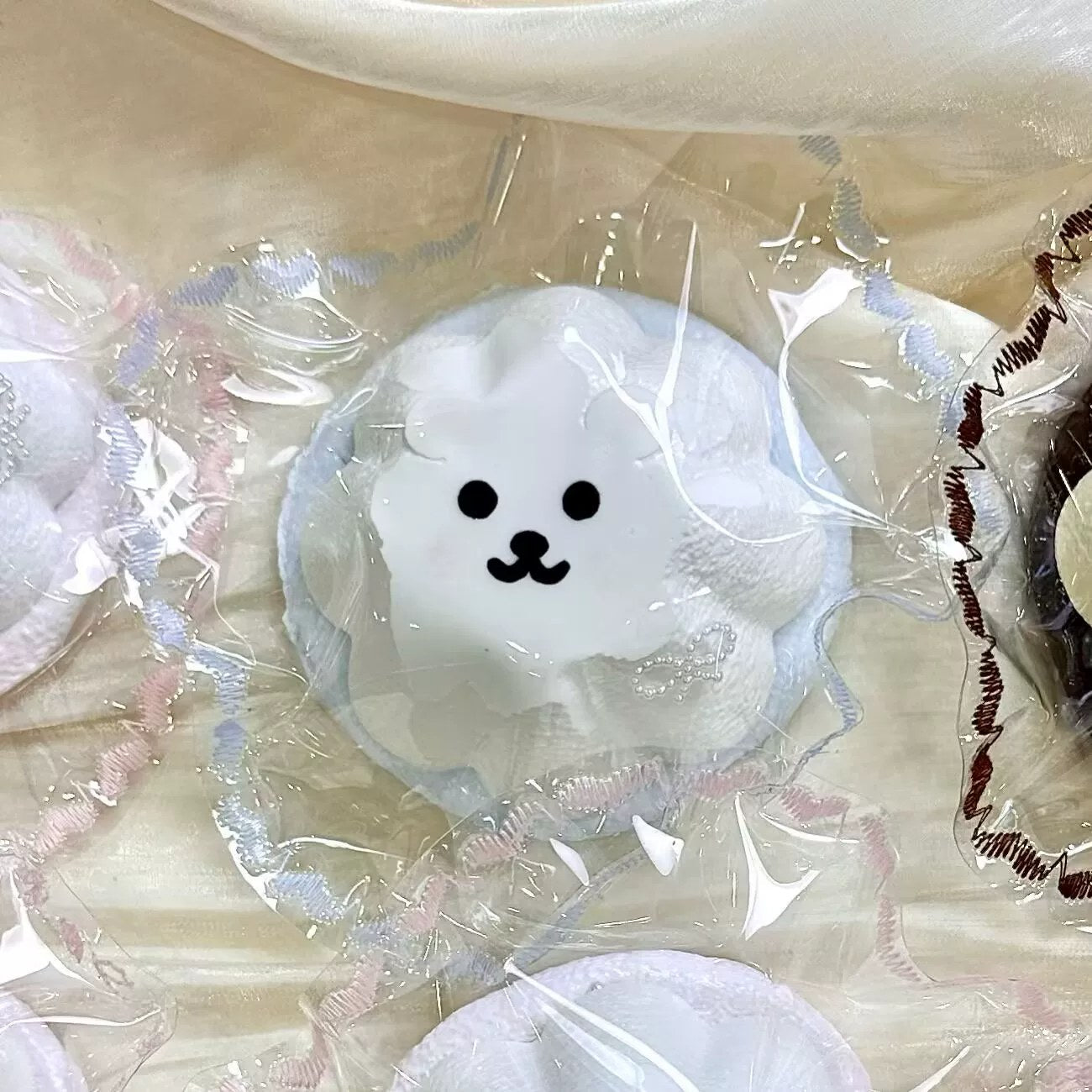 White pudding-shaped squishy with a small black face in clear packaging.